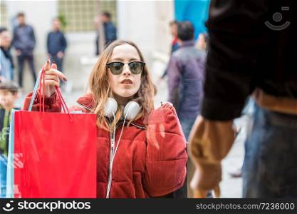 Beautiful attractive young girl in jumper with headphone and sunglasses looks at clothes display windows at shopping store