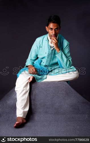 Beautiful authentic Indian hindu man in typical ethnic groom attire sitting and thinking on top of pyramid rock. Bangali male wearing a light blue agua decorated Dhoti with shawl.