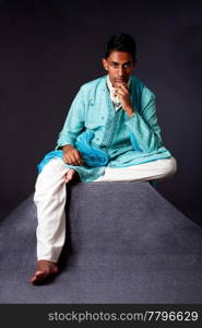 Beautiful authentic Indian hindu man in typical ethnic groom attire sitting and thinking on top of pyramid rock. Bangali male wearing a light blue agua decorated Dhoti with shawl.