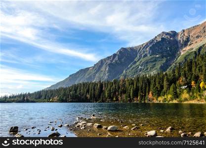 Beautiful autumn mountain landscape with a lake and a forest at the foot of rocky mountains against the blue sky