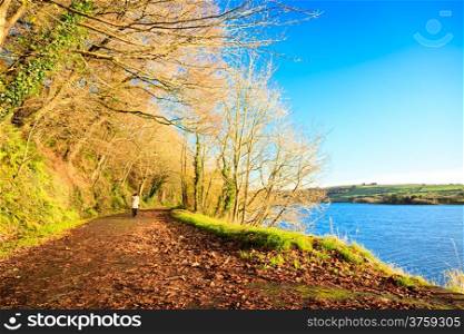 Beautiful autumn pathway. Co.Cork, Ireland Europe. Woman walking relaxing outdoor. Sunny day orange fall leaves.