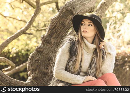 Beautiful autumnal woman in park. Young beauty woman wearing stylish autumnal clothes sitting and relaxing in park. Fashionable caucasian girl student resting on air.