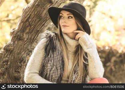 Beautiful autumnal woman in park. Young beauty woman wearing stylish autumnal clothes sitting and relaxing in park. Fashionable caucasian girl student resting on air.
