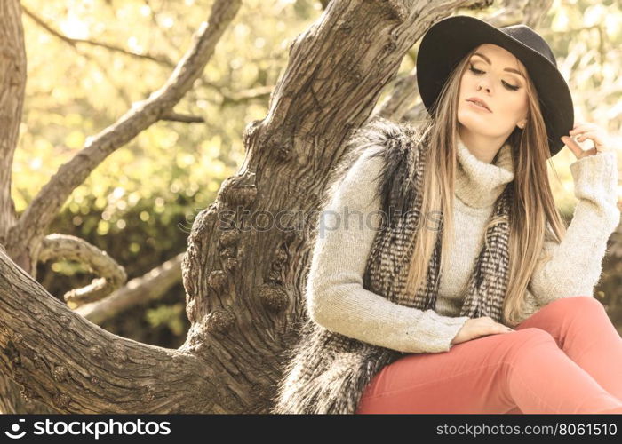 Beautiful autumnal woman in park. Young beauty woman wearing stylish autumnal clothes sitting and relaxing in park. Fashionable caucasian girl student resting on air.