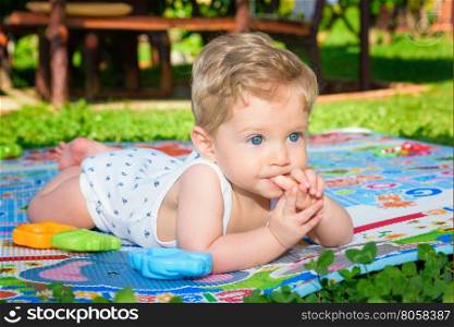 Beautiful baby boy eight month old crawling in the garden with finger in mouth ,close up.