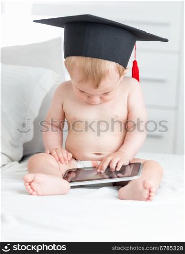 Beautiful baby boy in graduation cap using digital tablet