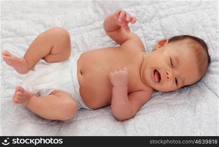 Beautiful baby in diaper lying on a gray blanket crying