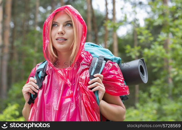 Beautiful backpacker in raincoat looking away at forest