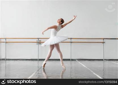 Beautiful ballerina rehearsal in ballet class, barre and white wall on background
