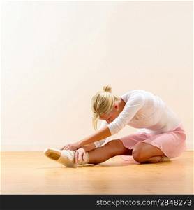 Beautiful ballerina warming up on the floor bending on knee