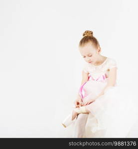 Beautiful ballet dancer isolated on white background. A small ballerina dresses or takes off her pointe.
