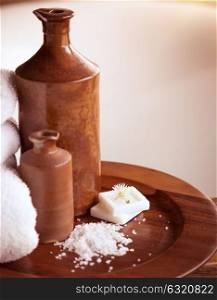Beautiful bathroom still life, two brown ceramic bottles on the wooden plate with sea salt and soap, spa and body care concept