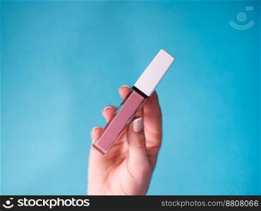 beautiful beige lip gloss in female hand isolated on blue background.