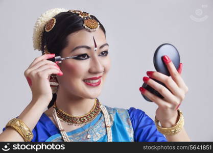 Beautiful Bharatanatyam dancer applying mascara over gray background