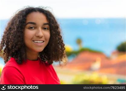 Beautiful biracial mixed race African American teenager teen girl young woman smiling with perfect teeth outside by the sea in summer