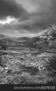 Beautiful black and white landscape image in Winter of Llyn Gwynant in Snowdonia National Park with snow capped mountains in background