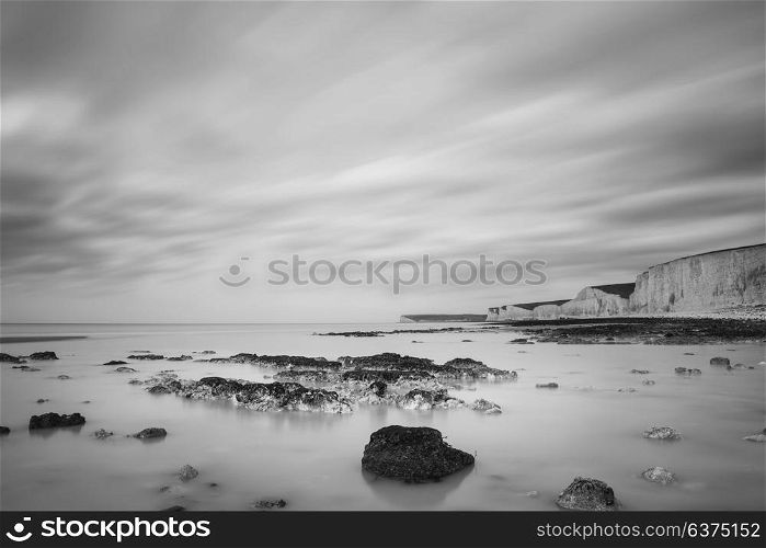 Beautiful black and white long exposure landscape image of low tide beach with rocks at sunrise