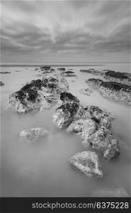 Beautiful black and white long exposure landscape image of low tide beach with rocks at sunrise