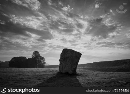 Beautiful black and white Summer sunrise landscape of Neolithic standing stones in English countryside with gorgeous light with background mist