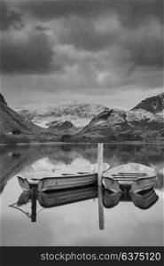 Beautiful black and white sunrise landscape image in Winter of Llyn Nantlle in Snowdonia National Park with snow capped mountains in background