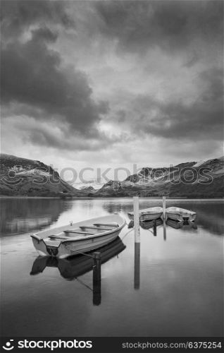 Beautiful black and white sunrise landscape image in Winter of Llyn Nantlle in Snowdonia National Park with snow capped mountains in background