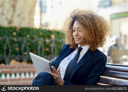 Beautiful black curly hair african woman using tablet computer in town. Businesswoman wearing suit with trousers and tie
