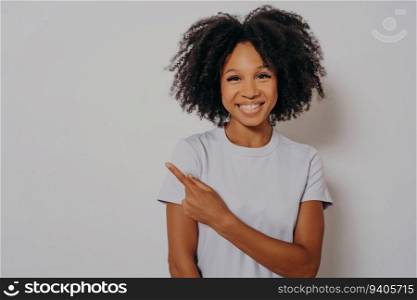 Beautiful black woman in casual clothes, beaming smile, points with hand and finger, happy expression