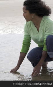 Beautiful black woman looking for shells in low water at the seaside