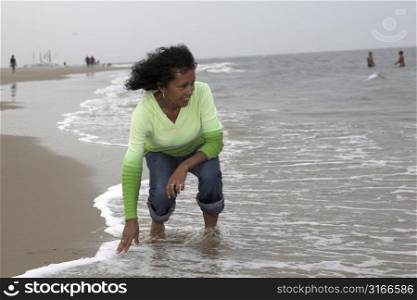 Beautiful black woman reaching down to feel the temperature of the water