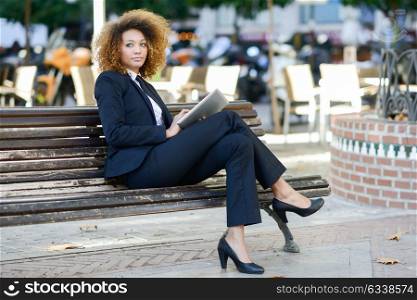 Beautiful black woman using tablet computer in urban background. Businesswoman wearing suit with trousers and tie, afro hairstyle.