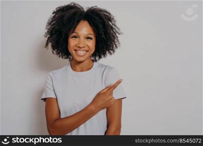 Beautiful black woman wearing casual clothes, cheerful with beaming smile on her face pointing with hand and finger up to side with happy and natural facial expression, copy space for advertising. Beautiful black woman cheerful with beaming smile on her face pointing with hand and finger up