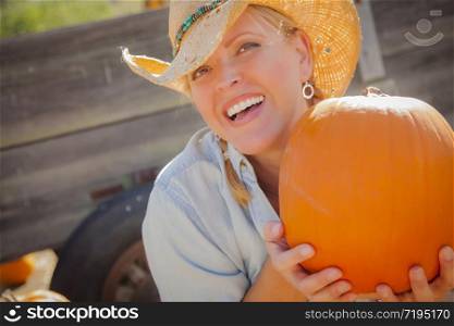 Beautiful Blond Female Rancher Wearing Cowboy Hat Holds a Pumpkin in a Rustic Country Setting.