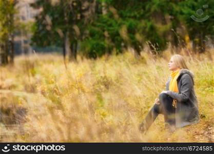 beautiful blond girl sitting on rivershore in autumn forest