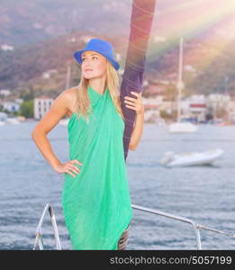 Beautiful blond girl standing on the deck of luxury sailboat in bright sun light, spending leisure time on the sea, enjoying summer vacation concept