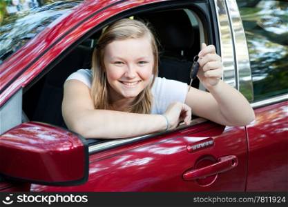Beautiful blond teenage girl sitting in her new car, holding the keys.