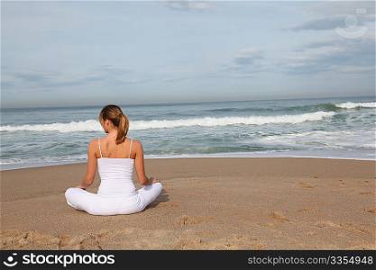 Beautiful blond woman doing stretching exercises on the beach