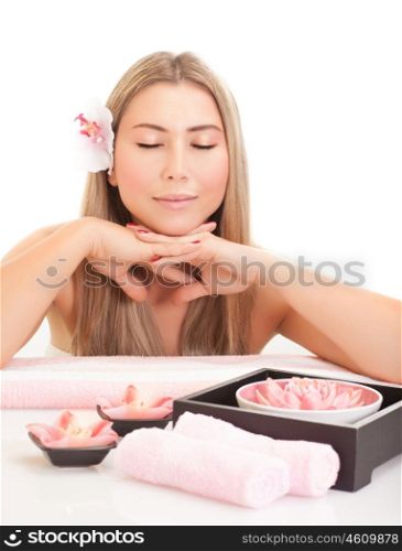 Beautiful blond woman enjoying dayspa, attractive female with pink orchid flower in head and gentle lotus flowers on the table in spa salon, beauty treatment concept