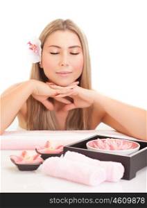 Beautiful blond woman enjoying dayspa, attractive female with pink orchid flower in head and gentle lotus flowers on the table in spa salon, beauty treatment concept