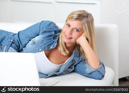 Beautiful blond woman laying on sofa with laptop computer