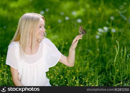 Beautiful blond woman playing with butterfly in spring park