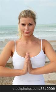 Beautiful blond woman practising yoga at the beach