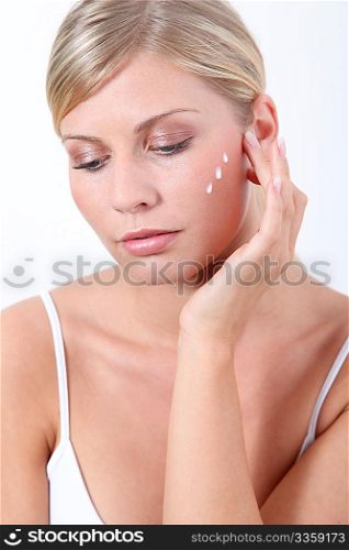 Beautiful blond woman putting facial moisturizer on her face