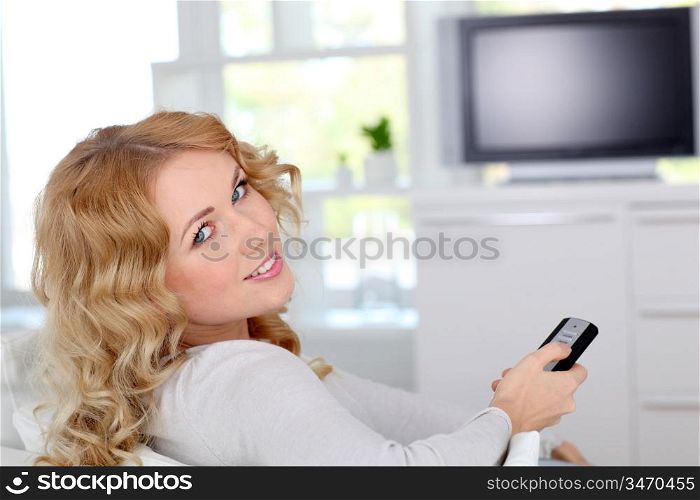 Beautiful blond woman sitting in sofa watching tv