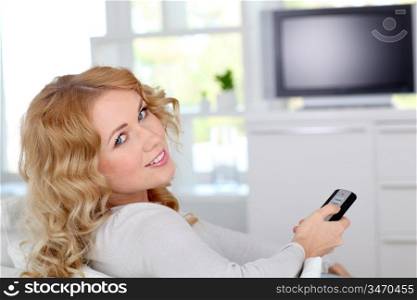 Beautiful blond woman sitting in sofa watching tv
