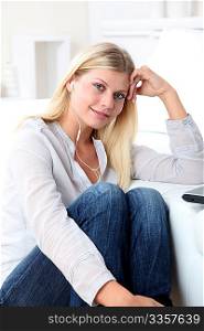 Beautiful blond woman with headphones sitting on sofa