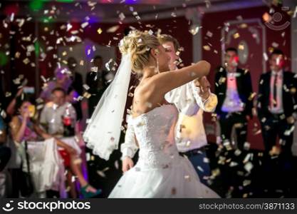 Beautiful blonde bride dancing at restaurant in flying confetti