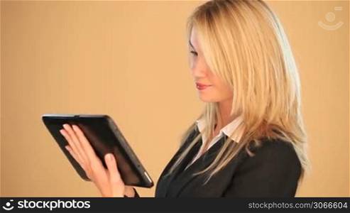 Beautiful blonde businesswoman working on a tablet looking up with a friendly smile against a brown background