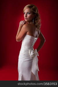 Beautiful blonde fashion model in white dress posing in studio over red background