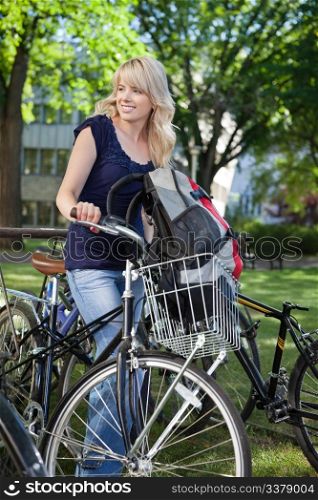 Beautiful blonde female student standing with her bike and looking away