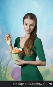 Beautiful, blonde, fresh woman with nice makeup and green dress. She has got bucket of easter eggs.